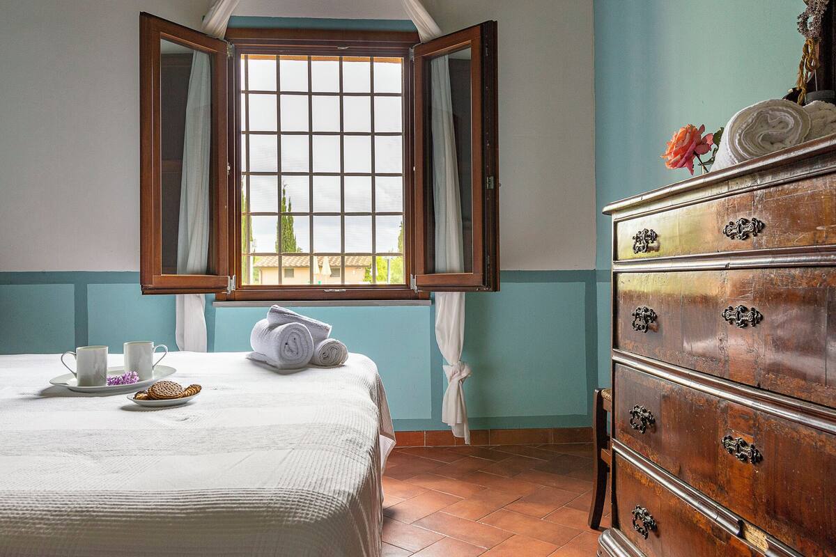 Une pièce avec un lit, une commode et une fenêtre dont les volets sont ouverts.
