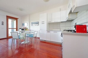 A modern kitchen with white cabinets, a red appliance, and a dining area with a glass table and chairs. - Modern flat with terrace near Eataly (Roma)