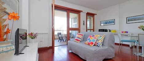 Una sala moderna con un sofá gris, almohadones coloridos, una mesa de centro blanca y un ventanal grande.