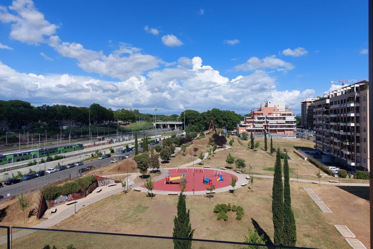 A park with playground equipment, a road with vehicles, and buildings in the background.