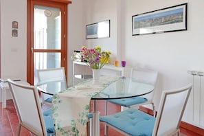 A dining area with a glass table, white chairs, and a vase of flowers. - Modern flat with terrace near Eataly (Roma)