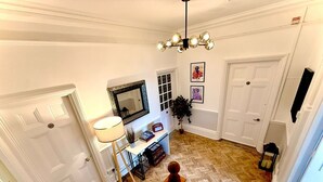 Un couloir avec un parquet à motifs en chevrons, une porte blanche, un bureau avec une lampe et un miroir.