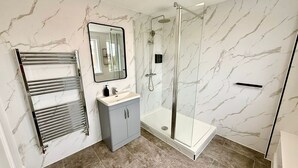 Une salle de bain dotée d’une douche à parois de verre, d’un sol carrelé en marbre et d’un meuble-lavabo avec un évier et un placard.