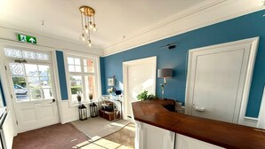 Une pièce avec un parquet en chevrons, un comptoir d’accueil en bois, une porte à cadre blanc et un mur bleu.