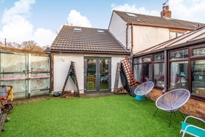 A residential property with a fenced backyard, a patio area with chairs, and a house with a tiled roof and large windows.