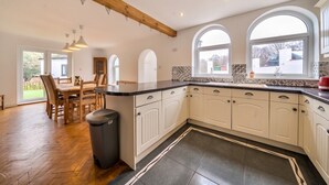 A kitchen with white cabinets, a wooden dining table, and a trash bin.