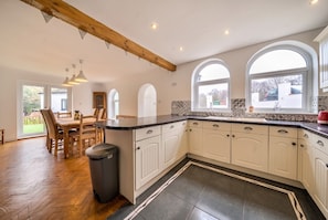 A kitchen with white cabinets, a wooden dining table, and a trash bin.