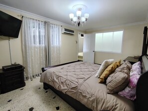 Quarto com cama, televisão, janela e ventoinha no teto.
