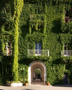 A building covered in green ivy with an arched entrance and potted plants at the base.