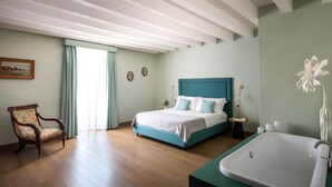 Ein Schlafzimmer mit Bett, Sessel, Badewanne und einem fenster mit Vorhängen.
