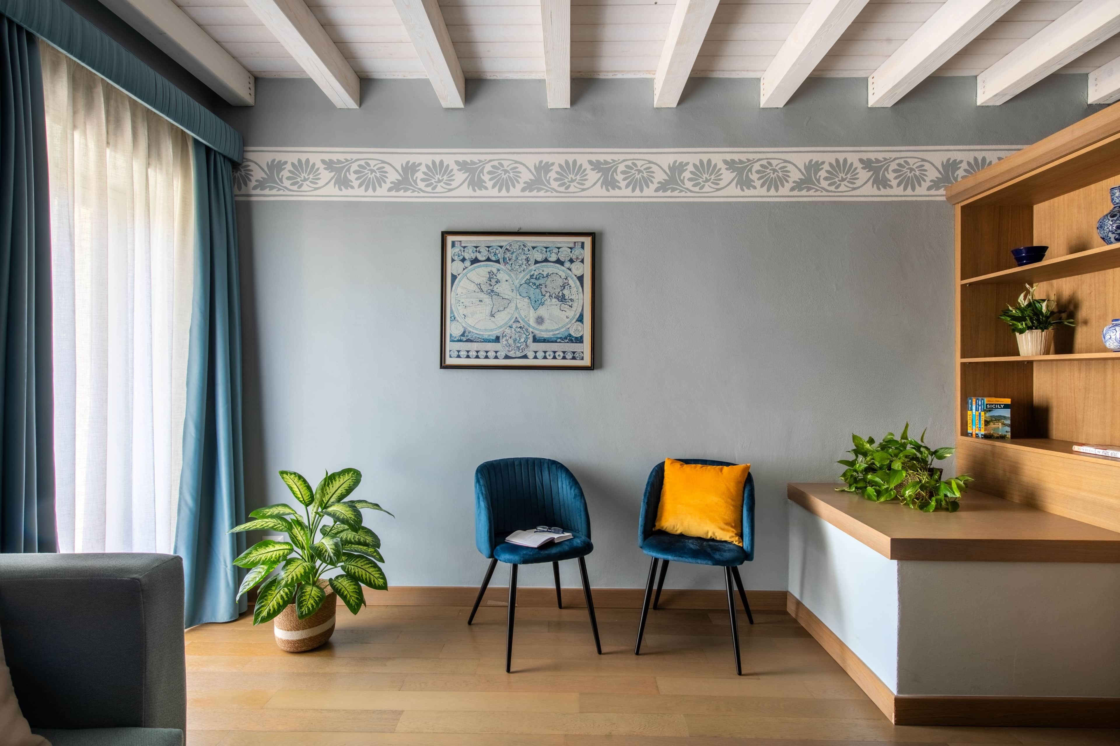 Un salon moderne avec un plafond en bois, un fauteuil bleu avec un coussin jaune, une table d’appoint en bois agrémentée de plantes et une carte du monde encadrée accrochée au mur.