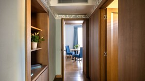 A hallway with wooden walls, a ceiling with decorative molding, and a view into a dining area with blue chairs and a table. - 103 Puccini Suite (Palermo)