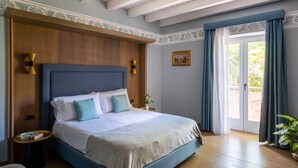 A bedroom with a large bed, wooden headboard, bedside tables, a nightstand, a potted plant, and a view of the outdoors through a door. - 103 Puccini Suite (Palermo)