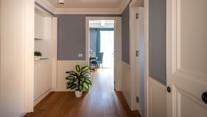 Un couloir avec des portes blanches, une plante en pot et une vue sur une salle à manger.