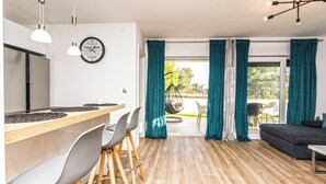 Een moderne keuken met een houten aanrecht en barstoelen, een eethoek met tafel en stoelen, en een woonkamer met bank en televisie.