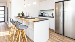 Een moderne keuken met een centraal kookeiland, barstoelen, roestvrijstalen apparatuur en hanglampen.