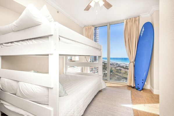 A bunk bed room with a large window, a surfboard, and a view of the ocean.