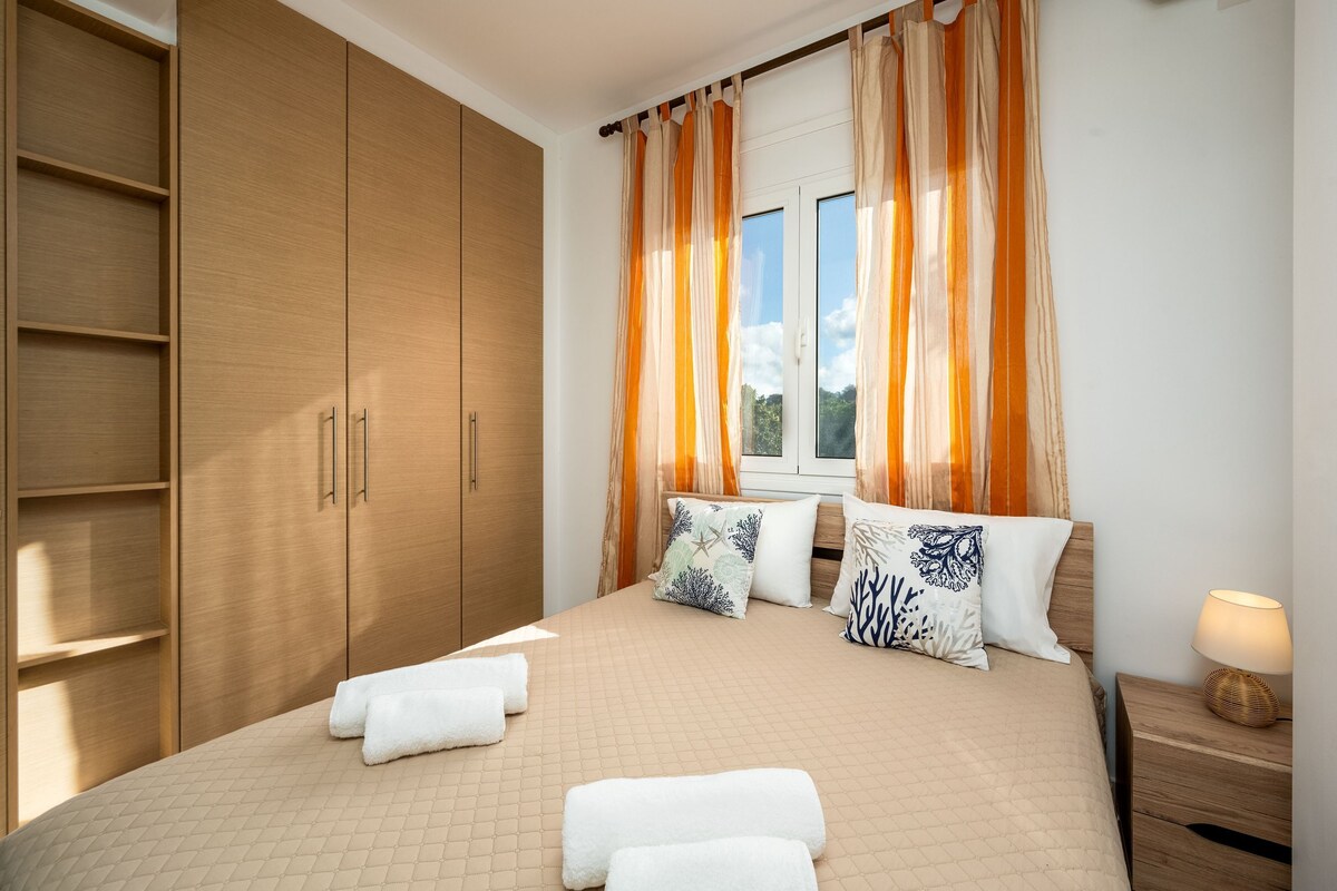 A bedroom with a large wardrobe, a bed with multiple pillows, and a nightstand with a lamp.