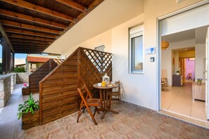 Eine Holztreppe führt zu einem Balkon mit Tisch, Stühlen und einem Blumentopf, mit Blick ins Freie.