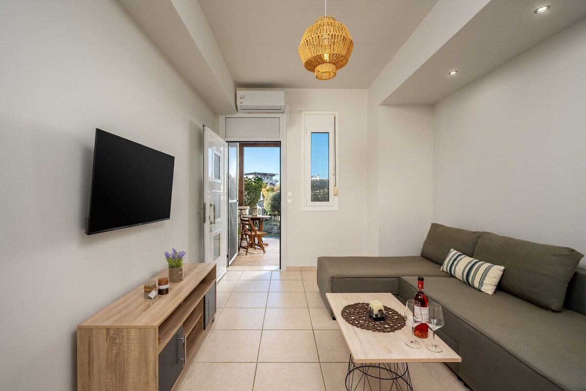 A modern living room with a flat-screen TV, a wooden console table, a grey sofa, and a dining area with a table and chairs.