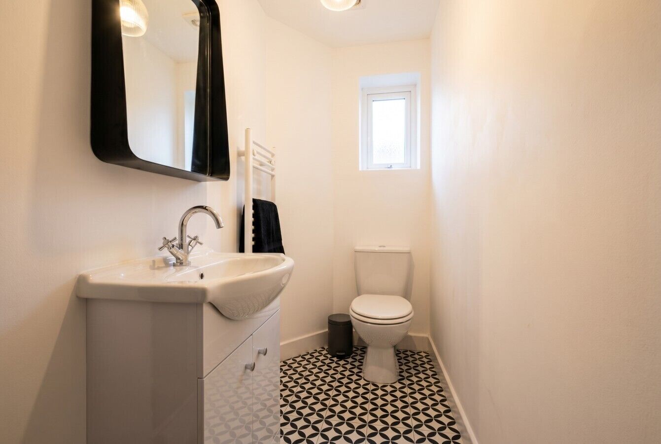 Et badeværelse med et hvidt håndvask, spejl og toilet.