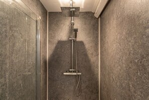 Ducha con cabezal de ducha de mano, panel de control en la pared y zona de ducha con mampara de cristal.