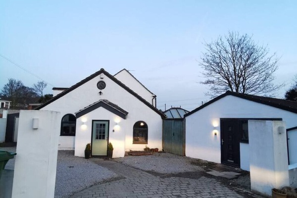 White outbuilding and neighbouring buildings with a shared driveway and paved parking area.