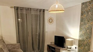 Een woonkamer met een bank, een televisie, een lamp en een kamerbreed gordijn.