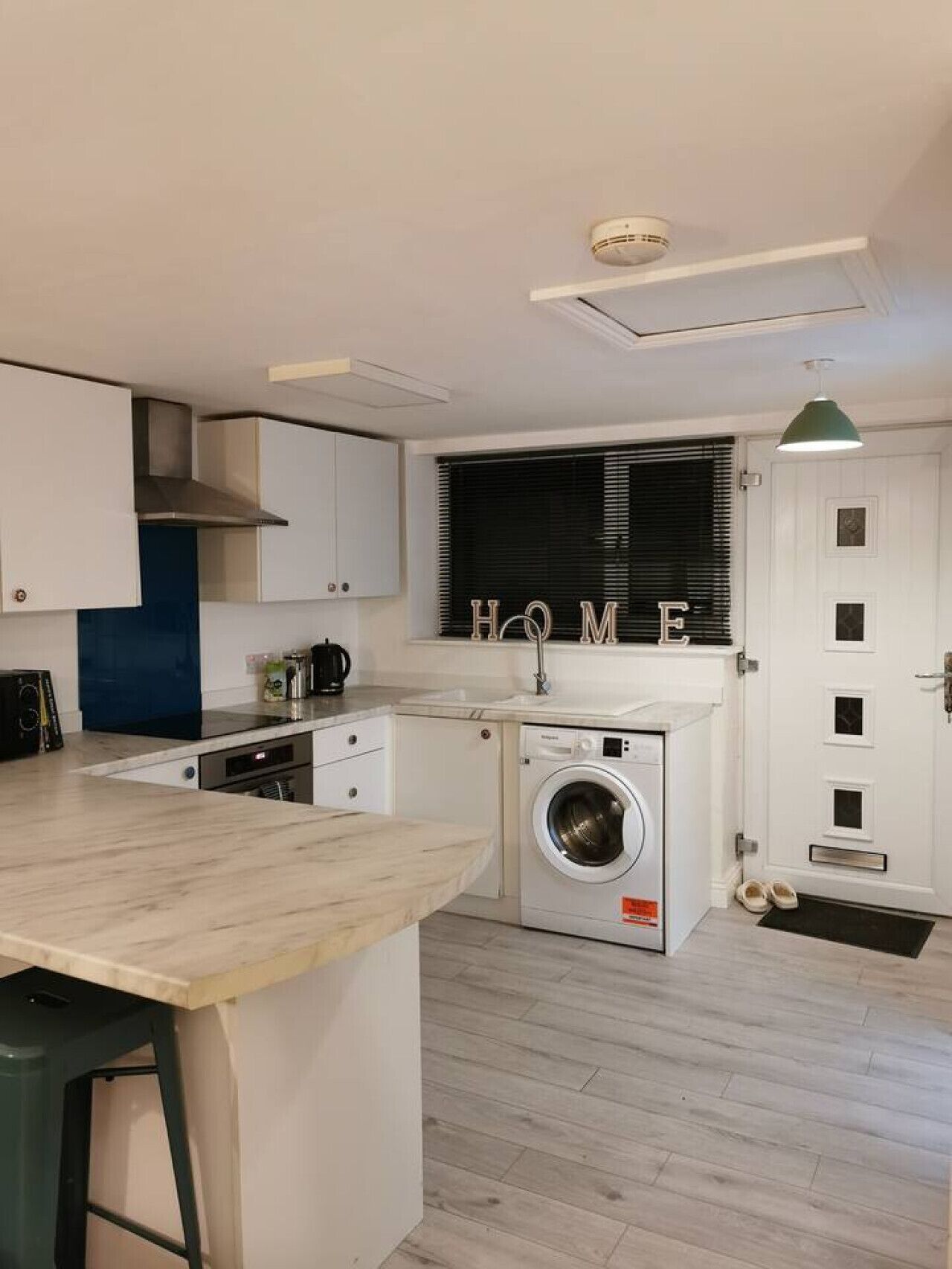 A compact kitchen with a built-in washing machine, a sink, and a window with blinds.