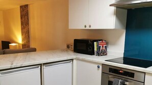 Een compacte keuken met witte kastjes, een magnetron, een inbouwoven en een blauwe achterwand.