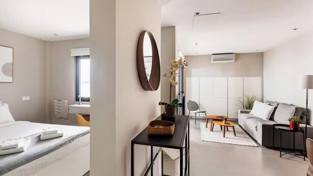 Ein modernes Hotelzimmer mit Bett, Nachttisch und großem Spiegel. Es gibt einen Wohnbereich mit Sofa, Couchtisch und einem kleinen Beistelltisch.