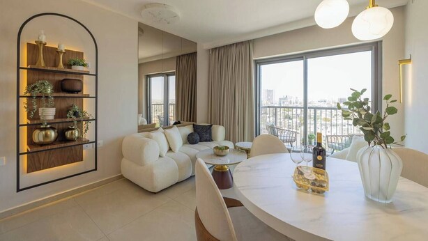 Een moderne woonkamer met een witte bank, een eettafel met een fles en glazen, en een groot raam met uitzicht op de stad.