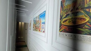 Un couloir orné d’affiches encadrées représentant l’Algérie et le couscous, un luminaire moderne et un plancher en bois.