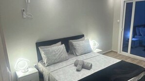 Une chambre à coucher avec un lit, des tables de chevet et une vue sur l’extérieur, accessible par une porte coulissante.