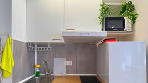 Una cocina compacta con armarios blancos, un lavamanos de acero inoxidable, un microondas, una estufa y un refrigerador.