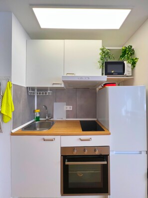 Eine kompakte Küche mit weißen Schränken, einer Edelstahl-Spüle, einer Mikrowelle, einem Herd und einem Kühlschrank.