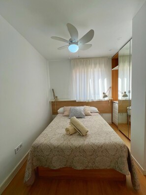 A bedroom with a bed, a ceiling fan, a window with curtains, a bedside table with lamps, and a mirror. - Congreso Apartment - Central by Residea (Torremolinos)