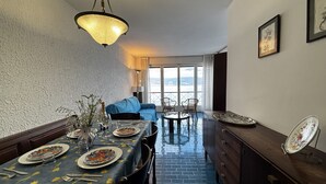 Ein Essbereich mit einem Tisch für zwei Personen, einem blauen Sofa und Meerblick durch große Fenster.