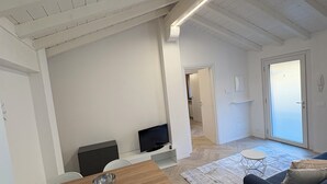 A spacious living area with a wooden dining table, two white chairs, a dark blue sofa, and a flat-screen TV. - Sweet & home 3 Apartment Delux near Bergamo (Azzano San Paolo)