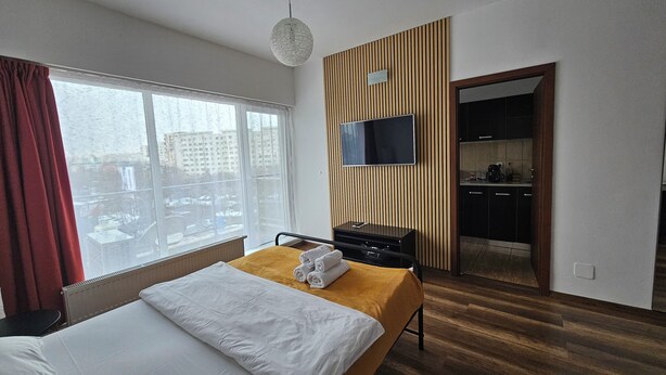 Habitación de hotel con una cama, televisión, pared de paneles de madera y vista a la ciudad por la ventana.