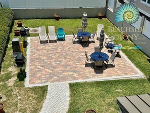 A patio area with a patterned tile floor, outdoor furniture including chairs and tables, and potted plants. - Beach Club 136: 1  BR, 1  BA Condominium in Tybee Island, Sleeps 4 (Tybee Island)