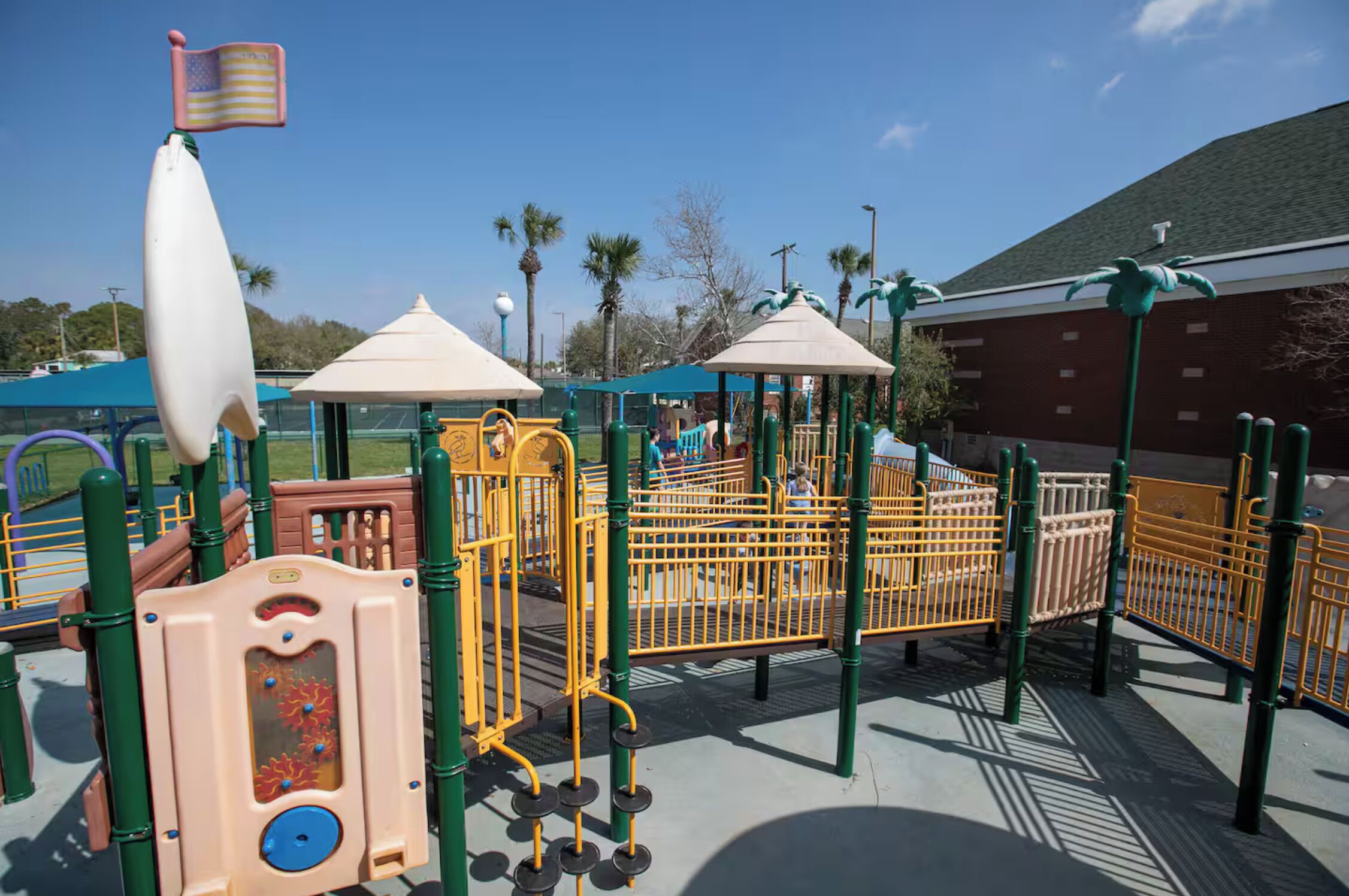 A playground with various play structures, including a climbing area and a slide, surrounded by safety railings.