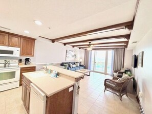 A modern kitchen with wooden cabinets, a central island, and a dining area with a sofa and wicker furniture.