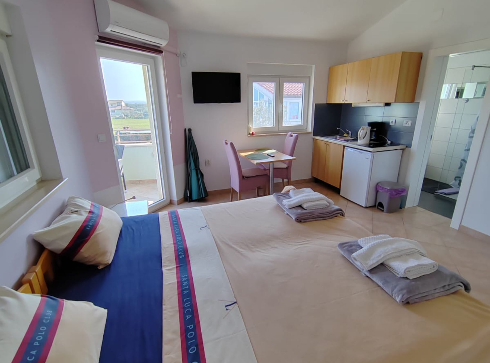 A bedroom with a bed, a desk, and a kitchenette.