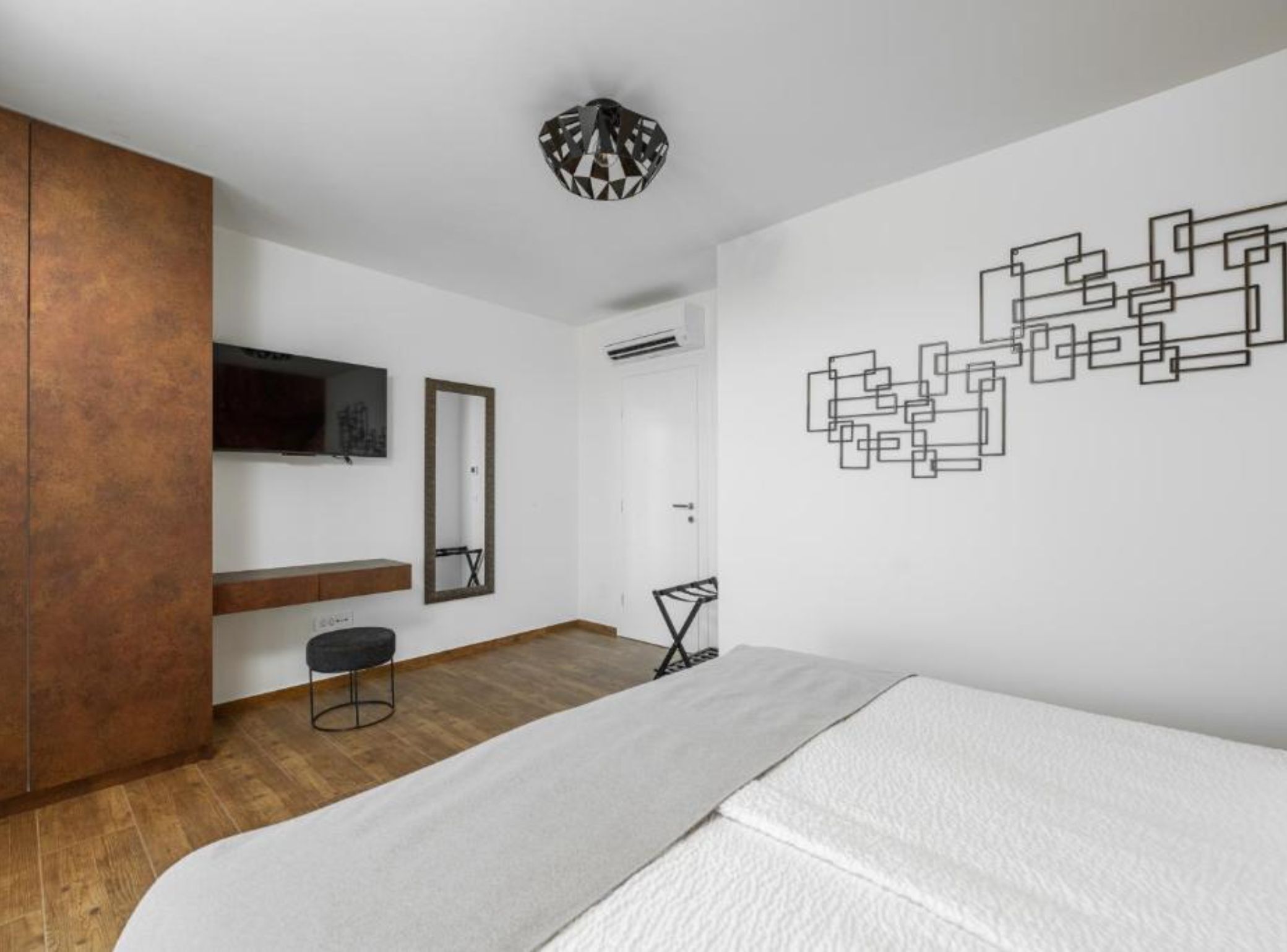 Une chambre moderne avec une armoire en bois, un lit, un bureau et une œuvre d’art murale.