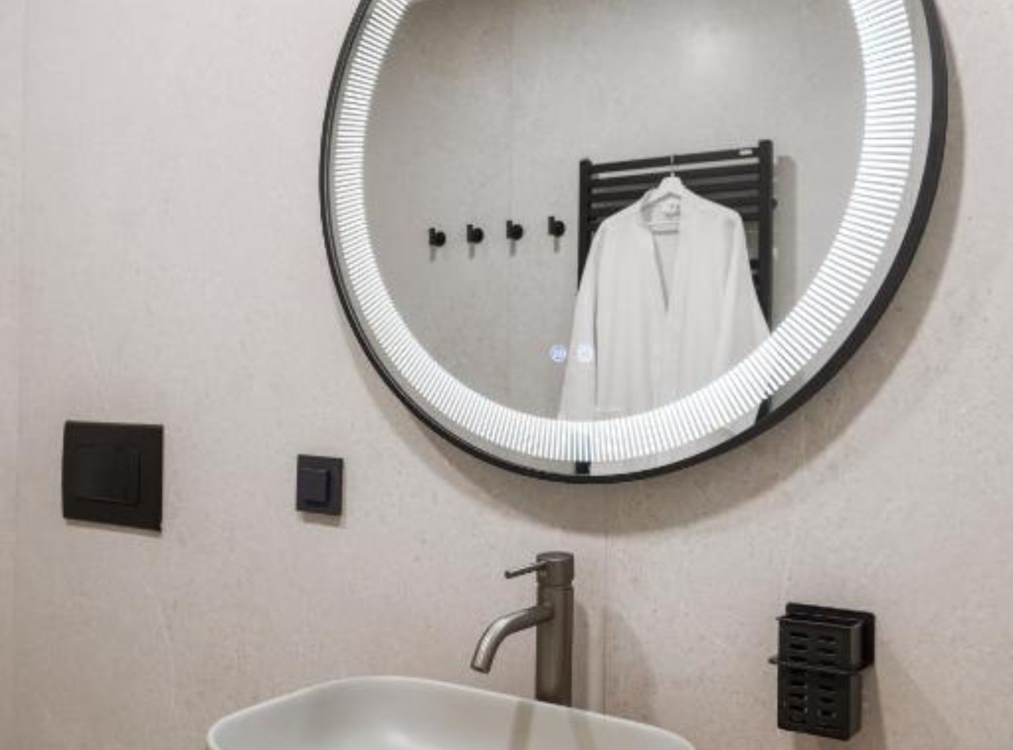 A bathroom with a round mirror, a sink, a towel rack, and a ventilation unit.