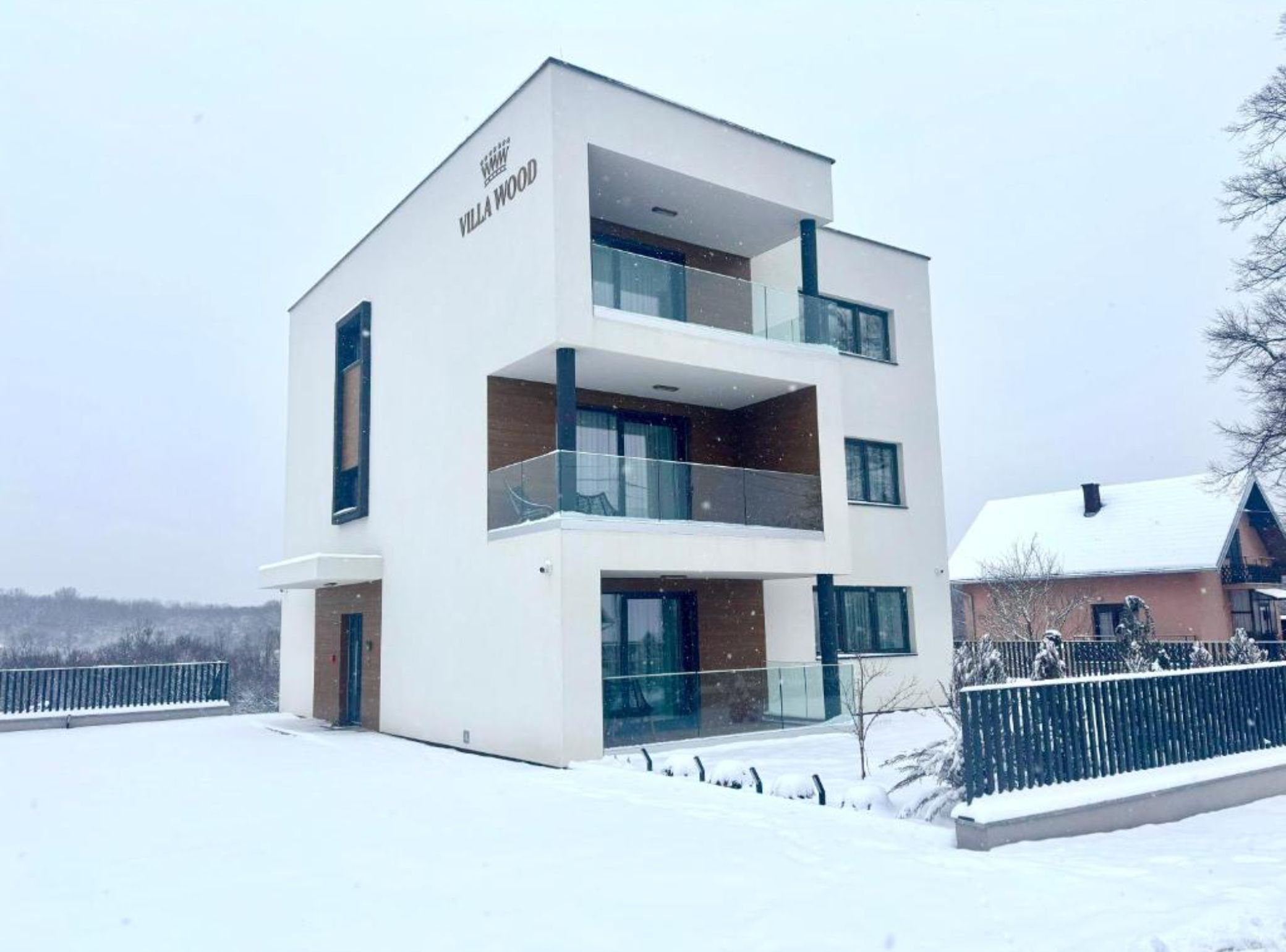 Un immeuble moderne à plusieurs étages, appelé Villa Wood, avec une façade blanche et de grands balcons en verre.