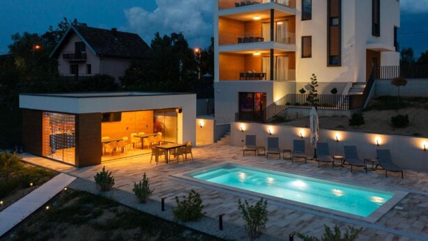 A modern multi-story building with a pool area, outdoor seating, and a well-lit entrance. - Apartments Villa Wood (Ivanic-Grad)