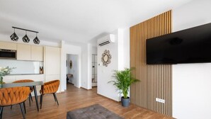A modern living space with a dining area, a grey sofa, and a flat-screen TV mounted on a wooden panel wall. - Apartments Villa Wood (Ivanic-Grad)