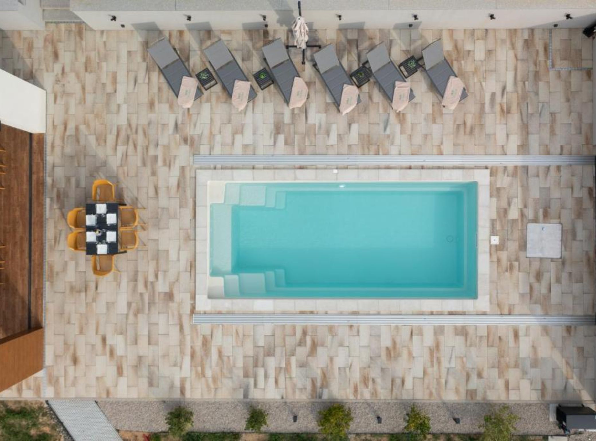 Un área de piscina en la azotea con una piscina rectangular, sillas de descanso y una mesa con sillas.